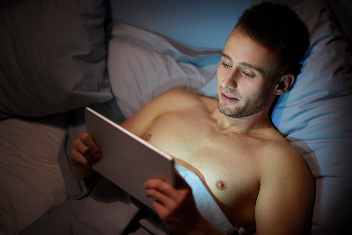 Man lying in bed using a tablet in a dimly lit room